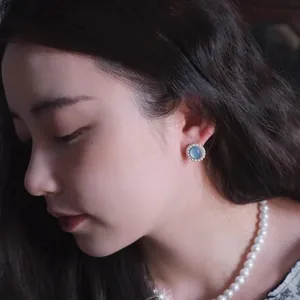 Detailaufnahme eines blauen Katzenaugen-Ohrrings mit Perlen am Ohr eines Models
