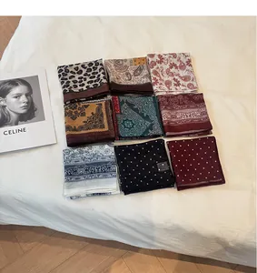 Divers petits foulards carrés en coton et lin à motifs dans une grille 3x3 sur tissu blanc.