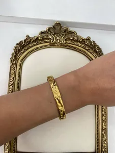 Macro view of a gold stainless steel C-shaped bangle featuring engraved star and flower motifs