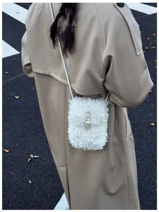 Close-up of a white fluffy faux fur crossbody bag worn over a beige trench coat