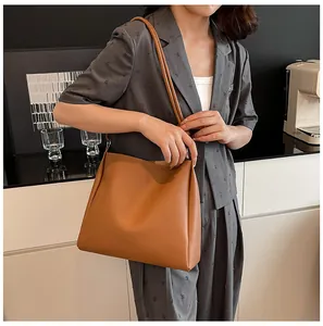 Model wearing a grey blazer carrying a large vintage brown leather shoulder tote bag
