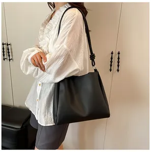 Large black minimalist tote bag carried by a fashion model in an indoor home setting.