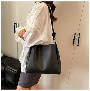 Side view of a large black matte leather tote bag with knot detail worn by a model