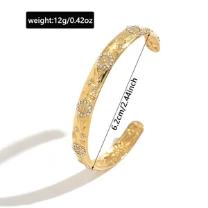 Close-up of gold stainless steel open bangle with flower and star patterns and dimensions