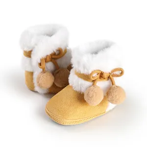 Soft sole baby booties in yellow faux suede featuring white faux fur and pom-poms.