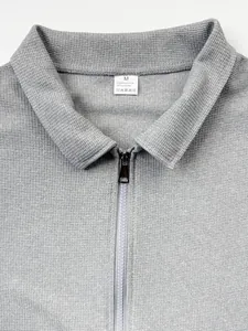 Détail d'une veste polo grise gaufrée avec fermeture éclair et étiquette de taille M