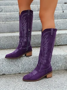 Close-up detail of stylish purple suede Western cowboy boots with white embroidery on stone stairs.