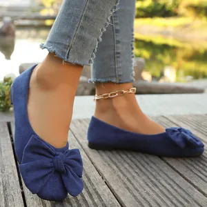 Dettaglio di ballerine piatte in camoscio blu da donna con un grande fiocco sul davanti.