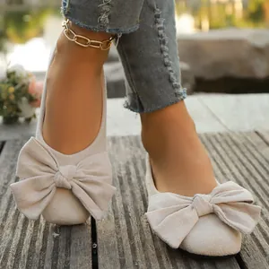 Primo piano di eleganti scarpe basse beige da donna con grandi fiocchi decorativi su legno