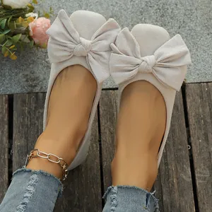 Dettaglio di ballerine in camoscio beige con grande fiocco decorativo da donna.