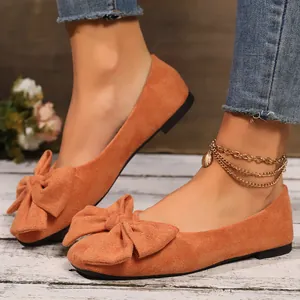 Primo piano di eleganti ballerine in pelle scamosciata arancione con decorazione a fiocco.