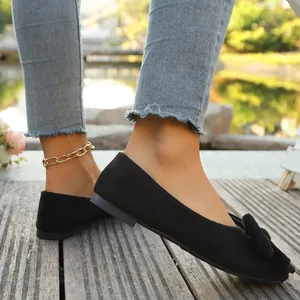 Primo piano di eleganti ballerine in camoscio nero con un fiocco di tendenza su legno