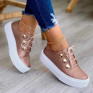 Sneakers platform oro rosa con bottoni dorati decorativi su un pavimento in legno.