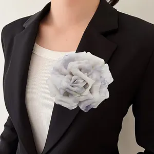 Dettaglio di una grande spilla a forma di camelia in tessuto bianco con motivi floreali.