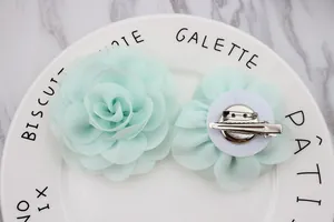 Detalle de broche de rosa de gasa verde menta con pinza y aguja de doble uso al dorso