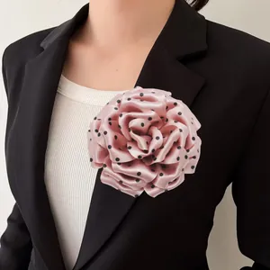 Elegant detail of a pink polka dot fabric peony flower brooch pinned on a black blazer jacket.