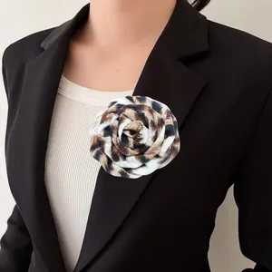 Dettaglio di spilla a forma di rosa in tessuto leopardato su blazer nero.