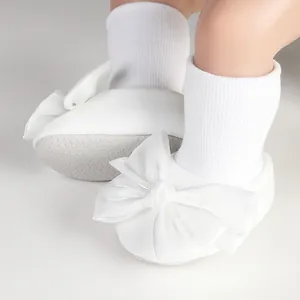 Detailed view of white baby floor socks featuring a large satin bow and non-slip sole