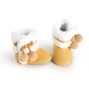 Detail view of yellow baby winter boots with soft white faux fur lining and pom-poms