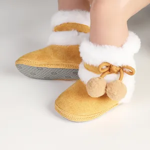 Detailed view of yellow winter baby boots with white faux fur and pom-poms