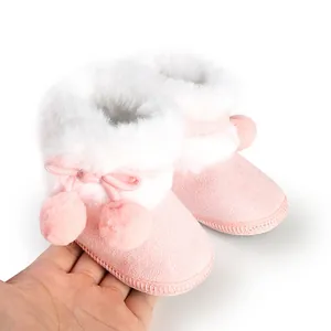 Close-up of warm pink baby winter boots with soft white faux fur and cute pom-poms