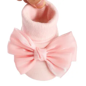 Macro detail of soft pink knitted baby socks featuring a decorative oversized satin bow