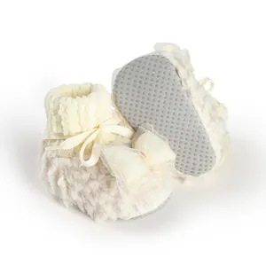 Detailed macro view of soft fuzzy baby winter booties with bow decoration and anti-slip sole.