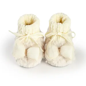 Close-up of warm cream fuzzy baby booties with elegant mesh bow and lace-up design.