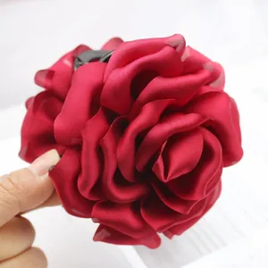 Detailed close-up of a large red silk rose hair claw clip showing fabric petal textures.