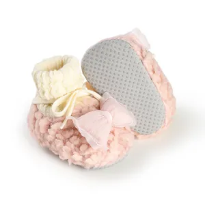 Detailed view of pink fuzzy winter baby booties with decorative bow and non-slip soles.