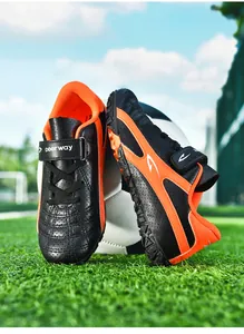 Détail en contre-plongée de chaussures de foot enfant noir et orange sur terrain vert