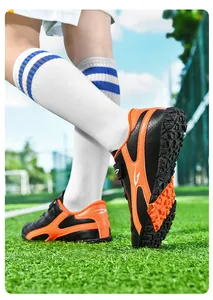 Vue détaillée de chaussures de football pour enfants noires et orange sur herbe