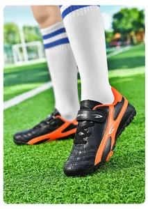 Détail en gros plan de chaussures de football pour enfants noires et oranges sur gazon