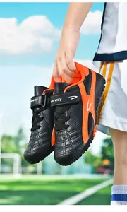 Vue détaillée de chaussures de football pour enfants noir et orange sur un terrain