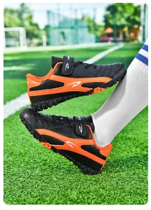 Gros plan de chaussures de football pour enfants noir et orange sur gazon artificiel