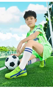 Jeune garçon portant un maillot de foot vert et des chaussures de foot vert citron sur terrain.