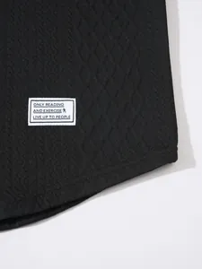 Close-up detail of a white woven text patch on the hem of a black textured knit sweater