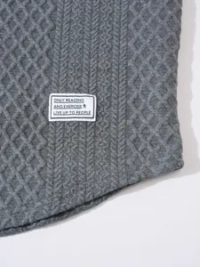 Detail shot of grey cable knit sweater with textured pattern and decorative label