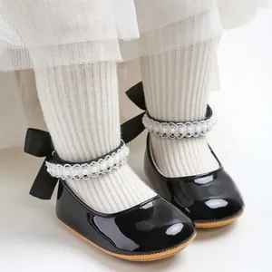Close-up detail of black patent leather baby princess shoes with pearl strap and heel bow.