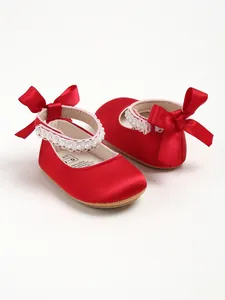 Close-up of red satin baby girl shoes featuring elegant bows and delicate pearl trim