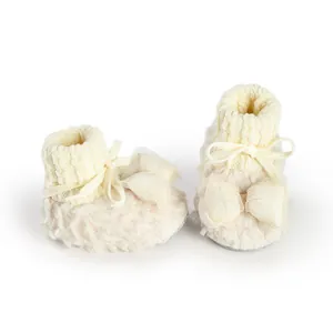 Close-up of fluffy cream baby booties with knit cuffs and decorative mesh bows