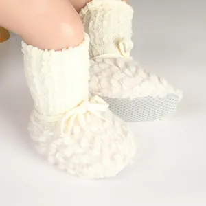 Detail shot of cozy white plush baby booties featuring knit cuffs and non-slip dotted soles