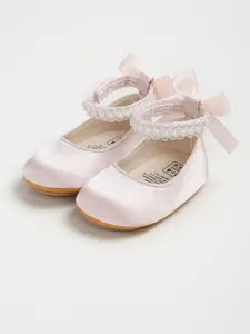 Close-up detail of pink satin baby princess shoes featuring pearl straps and delicate ribbon bows