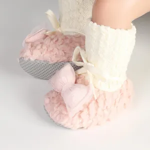 Close-up of pink fuzzy baby shoes with white cable knit socks and pink bow detail.