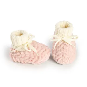 Close-up of cozy pink fuzzy baby booties with cream knitted ankle cuffs and bow