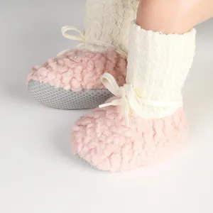 Close-up view of pink plush baby walker socks with white cable knit and decorative bow