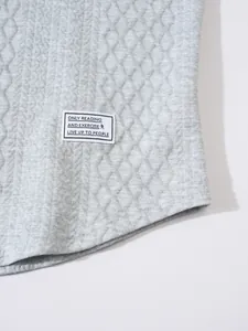 Close-up of grey quilted sweatshirt texture with decorative letter patch.
