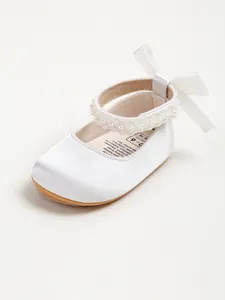 Close-up of white satin baby princess shoe featuring pearl strap and ribbon bow detail.