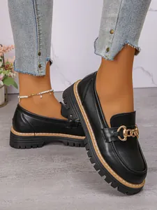 Close-up detail of black platform loafers with chunky lug sole and gold chain ornament