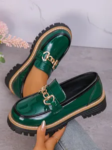Close-up of green patent leather chunky loafers with decorative gold chain detail